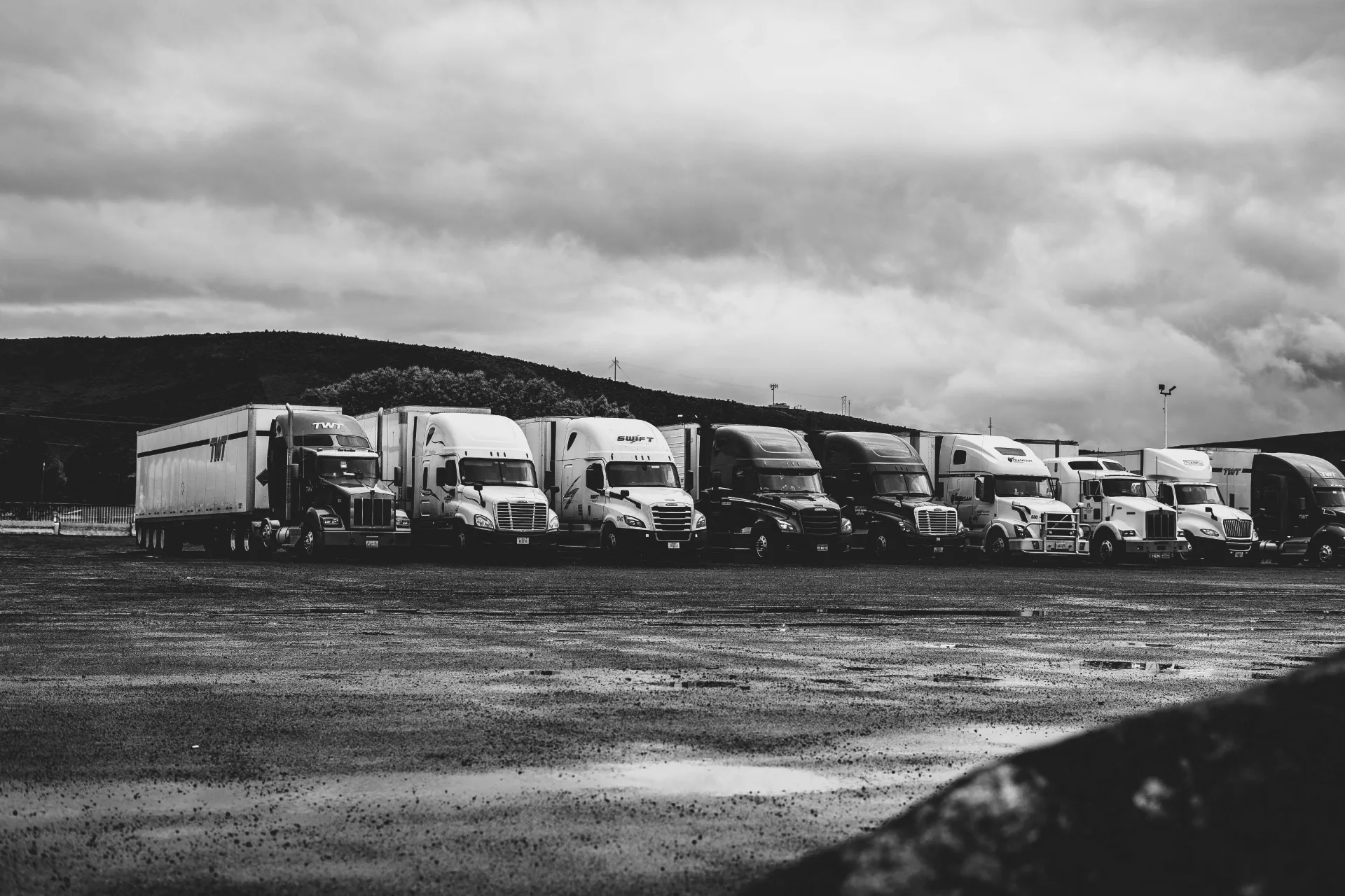 Fleet of semi trucks lined up in a yard under overcast skies